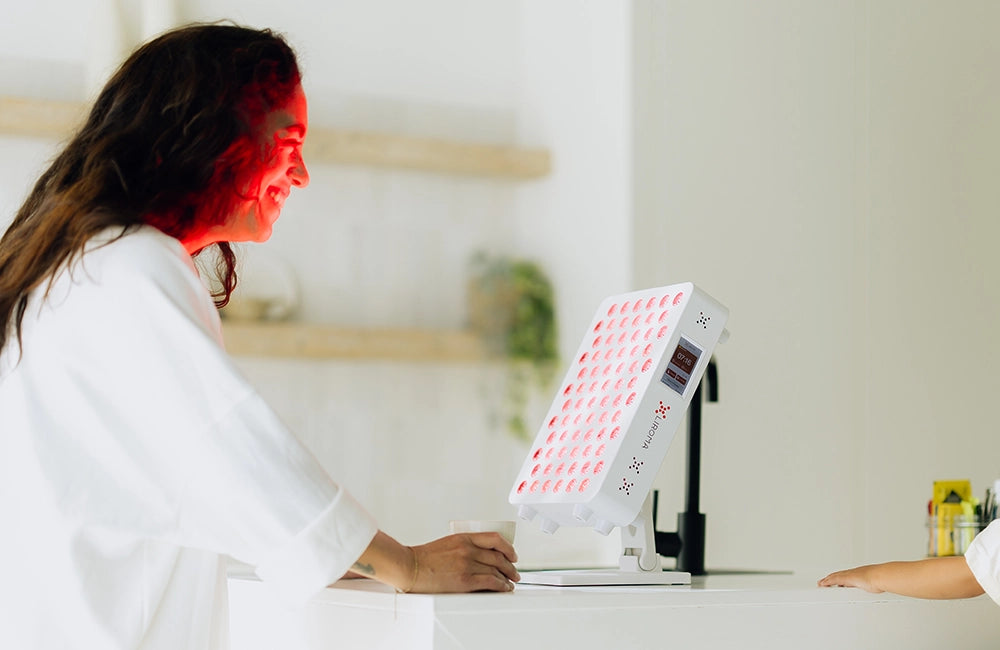Vrouw behandelt haar gezicht met de Liroma Compact rood licht lamp aan tafel